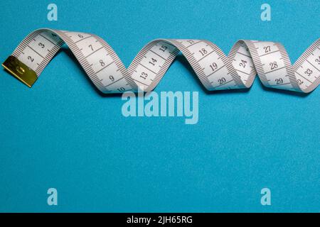 Top view of white soft measuring tape. Minimalist flat lay image of tape measure with metric scale over blue background. Composition photo of tape mea Stock Photo