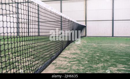 Net and a part of green synthetic grass paddle tennis court indoor without people. Paddle is a racquet game. Professional sport concept with copy spac Stock Photo