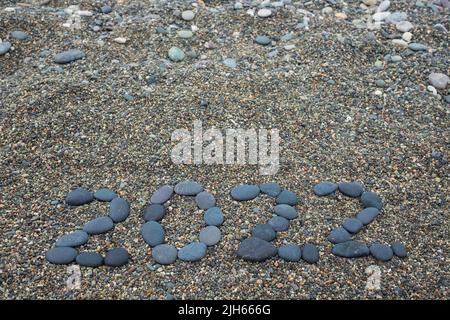 Year 2022 made from black stones on sandy beach. Stock Photo