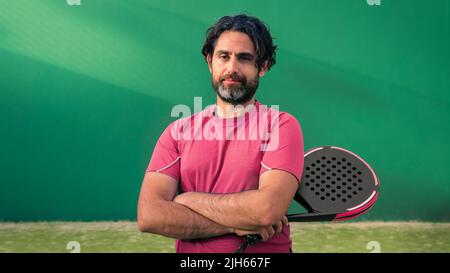 Monitor of padel holding black racket with copy space. Class to student on outdoor tennis court. Man paddel player playing a match in the open. Racque Stock Photo