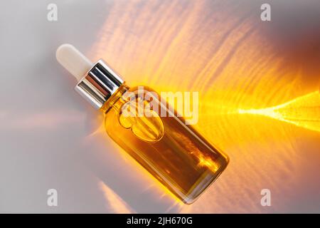 Mockup of glass dropper bottle with a metal cap and yellow essential oil on a background with an abstract fire pattern of light and shadow. Eco cream, serum, cosmetics, massage oil. Copy space Stock Photo
