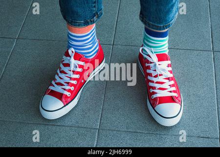 Kid wearing different pair of socks. Child legs in mismatched socks on gray background. Odd Socks day, Anti-Bullying Week. Down syndrome awareness Stock Photo