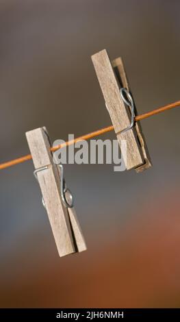 Closeup of two clothing pegs on a washing line outside against a blurred background. Wooden clothespins used to clip and hang clean laundry in the sun Stock Photo