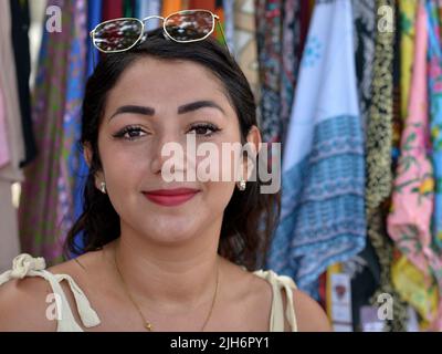 Attractive beautiful young Hispanic Latina Mexican brunette woman with eye makeup, red lipstick and modern eye brows wears her sunglasses on forehead. Stock Photo