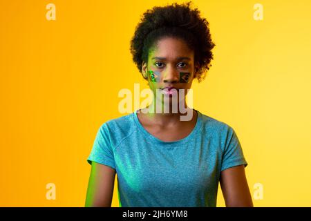 Image of african american female soccer fan with flag of portugal in yellow lighting Stock Photo