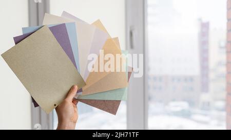 Woman holding fabric samples of roller blinds against window background.  Stock Photo