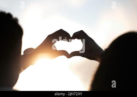 You make me whole. an unidentifiable couple making a heart shape with their hands at sunset. Stock Photo