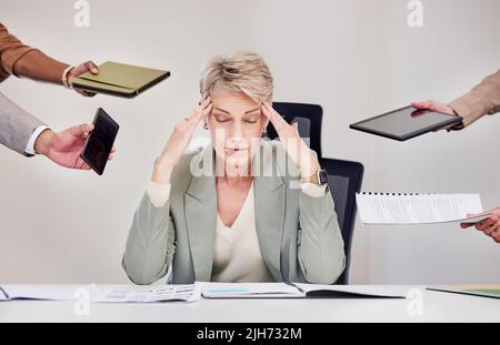 The joys of being their manager. a mature businesswoman sitting in the office and feeling stressed while her colleagues put pressure on her. Stock Photo
