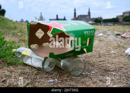 Dresden, Germany. 13th July, 2022. Empty wine bottles and the packaging of beer bottles lie at Palaispark on the Elbe meadows in front of the Old Town. After hot days and balmy summer nights, trash left behind by visitors piles up in public green spaces and parks. Credit: Robert Michael/dpa/Alamy Live News Stock Photo