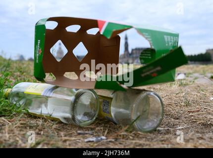 Dresden, Germany. 13th July, 2022. Empty wine bottles and the packaging of beer bottles lie at Palaispark on the Elbe meadows in front of the Old Town. After hot days and balmy summer nights, trash left behind by visitors piles up in public green spaces and parks. Credit: Robert Michael/dpa/Alamy Live News Stock Photo