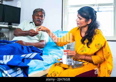 Daughter giving medicine or pills to admitted sick father at hospital - concept of family caring, medical treatment and health care. Stock Photo