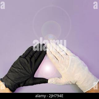 Hands with black and white gloves, united to form a triangle and in the center a soft luminous flash on a violet background, healing energy, triangula Stock Photo