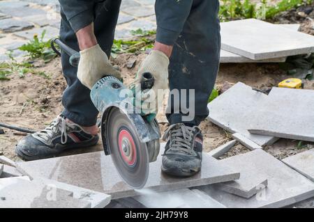 A worker with a circular saw cuts a tile in close-up. Stock Photo