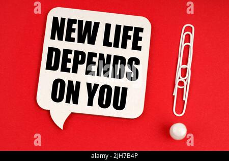 Business concept. On a red background, paper clips are an exclamation mark and a thought plate with the inscription - NEW LIFE DEPENDS ON YOU Stock Photo