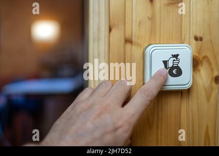 Hand of man turning on a light bulb with symbol of the high cost of electricity due to inflation. Stock Photo