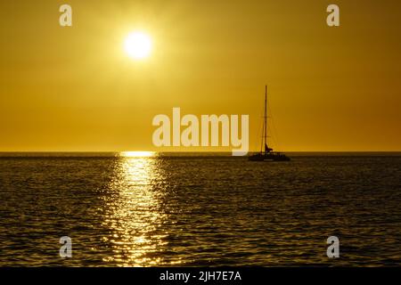 sunset in the sea with the sun on the horizon reflecting the light in the water and on the rocks on the shore. Gran Canaria. Spain Stock Photo