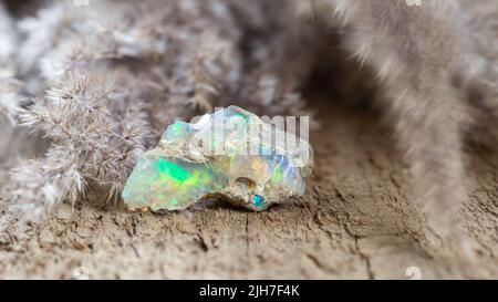 Shiny colorful boulder opal stone on wooden background . Rough unprocessed gemological sample of opal gem stone Stock Photo