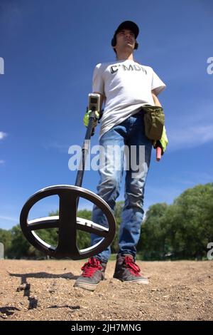 a guy in wireless headphones holds a wireless metal detector in his hand on the beach Stock Photo