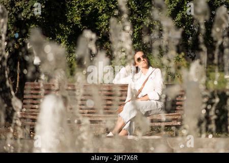 Portrait of a young woman as seen through fountain sitting on bench in the City Garden, Sofia, Bulgaria, Eastern Europe, Balkans, EU Stock Photo