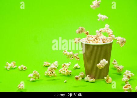 Popcorn is poured into a paper brown glass on a green background with place for text. Stock Photo