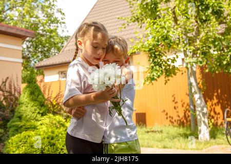A six-year-old boy gives a girl a bouquet of flowers. Sunny day, in the garden the boy gives a bouquet of daisies to the girl. Stock Photo