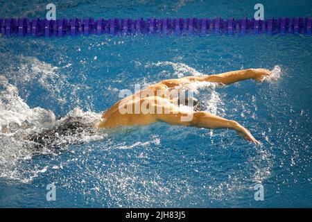 Details with a professional male athlete swimming in an olympic swimming pool butterfly style. Stock Photo