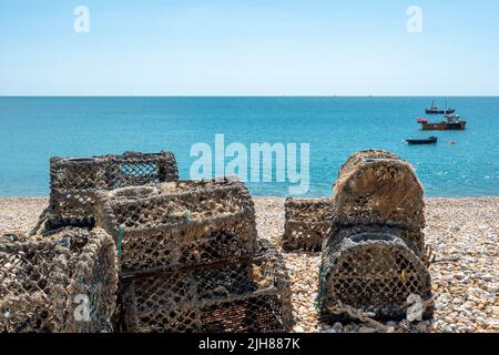 lobster pots traps on deserted beach at Selsey West Sussex England with the sea and fishing boats in the background Stock Photo