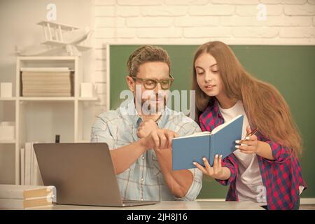 attentive teen girl and teacher man in high school with workbook and pc at blackboard, schoolwork Stock Photo