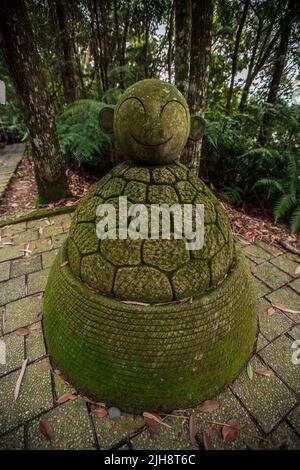 A vertical shot of a weathered green Stone Jizo of a smiling shape on stone floor in Wenwu Temple, Taiwan Stock Photo