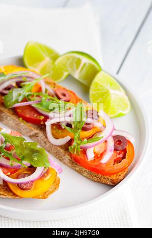 Vegetarian toasts and lime on a white plate. Bruschetta with tomatoes, greens and olives. Healthy open sandwiches on white boards. Top view Healthy ve Stock Photo