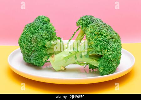 Two Fresh and Raw Pieces of Broccoli on White Plate. Uncooked Green Cabbage. Vegan and Vegetarian Culture. Raw Food. Healthy Eating and Vegetable Diet Stock Photo