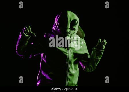 Futuristic alien showing frightening gesture, trying to scare. Creepy mask of humanoid on neon extraterrestrial planet masquerading as human person in Stock Photo