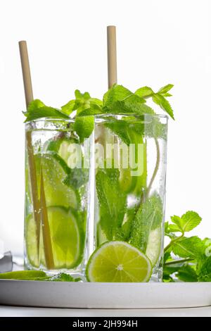 Mojito cocktail and bar tools on a white background. Two glasses of mojito with mint and lime on a white plate. Summer drink with bamboo straw Stock Photo