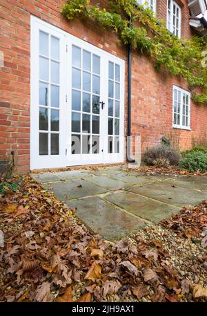 UK landscaped garden in Autumn with leaves, wooden French doors and a York stone patio Stock Photo