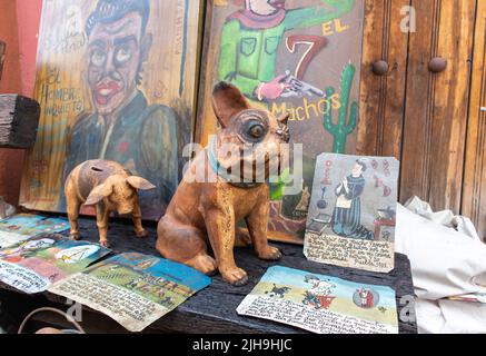 ceramic pottery dog at sale in a traditional mexican street market along with paintings catholic prayers with religious votive images and a piggy bank Stock Photo