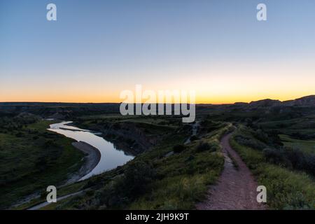 The sunset casts orange and yellow skies over the Missouri River at Theodore Roosevelt National Park in North Dakota Stock Photo