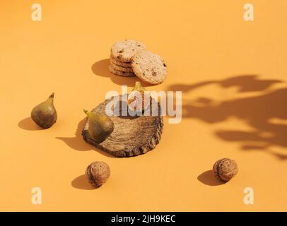 Vintage style composition made of figs on wooden podium, cookies and nuts on orange background. Retro style food concept. Stock Photo