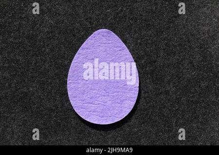 Single purple felt egg shape against dark grey felt background Stock Photo