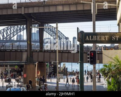 Tourists mill around Circular Quay with the Sydney Harbour Bridge in the background. The City Loop railway line and station are centre image. Stock Photo