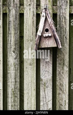 Old, wooden, and rustic bird feeder hanging on a fence in a backyard garden. Closeup of a vintage birdhouse on a wall outside. Built enclosures for Stock Photo