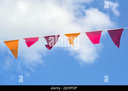 Pennants in warm colors hanging on a line between against a blue sky with clouds, decoration for a summer party or festival, copy space Stock Photo