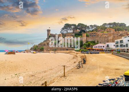 A colorful sky at dusk along the Platja Gran sandy beach with the 12th century fortified hilltop castle behind at the town of Tossa de Mar, on the Cos Stock Photo