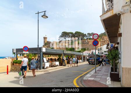 Waterfront and seaside sidewalk cafes along the sandy beach with the castle in view behind in Tossa de Mar, Spain, on the Costa Brava coastline. Stock Photo