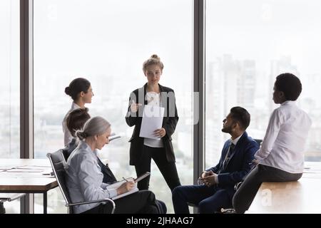 Young businesswoman presenting project report to different aged diverse team Stock Photo
