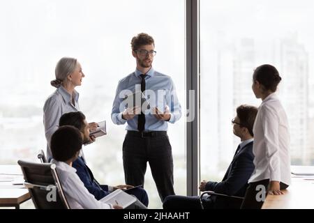 Confident young CEO man talking to team, speaking, instructing employees Stock Photo