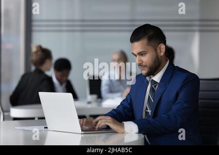Focused Indian employee man working on online project at laptop Stock Photo