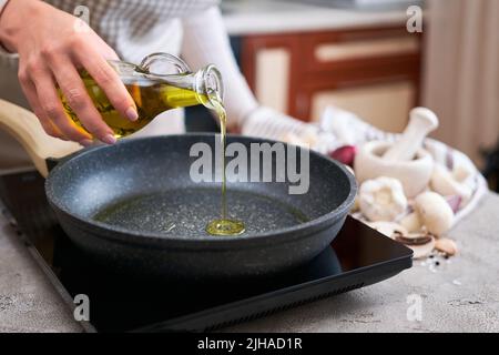 Woman pouring olive oil on frying pan at domestic kitchen Stock Photo