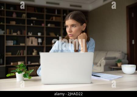 Young pensive businesslady distracted from laptop work staring into distance Stock Photo