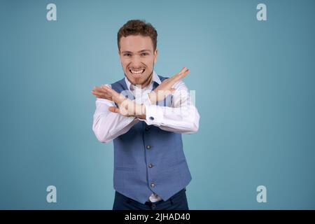 Portrait young business man with crossed arms, looking at camera, on blue background. Bearded guy in white shirt and blue vest posing in studio Stock Photo
