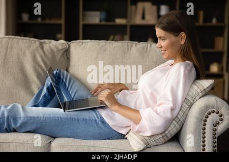 Pretty woman sits on couch in living room with laptop Stock Photo